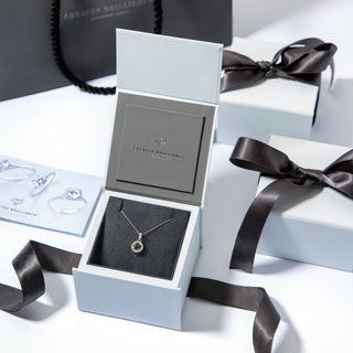 Jewelry box with a necklace featuring a green gemstone, surrounded by black ribbons on a white surface.