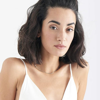 Woman with shoulder-length dark hair wearing a white top against a plain background