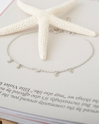 Silver bracelet with small charms on a book page with a starfish