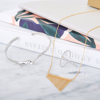 Gold necklace with geometric pendant on a marble surface