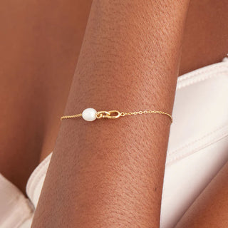 Gold bracelet with a pearl on a wrist against a neutral background