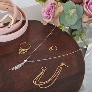 Gold and silver necklaces on a wooden surface with flowers in the background