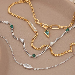 Three gold and silver chain necklaces with gemstone accents on a beige surface