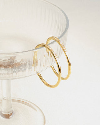 Two gold hoops on a clear glass surface with a white background