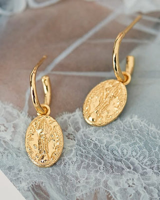 Gold earrings with intricate designs on a lace fabric background