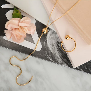 Gold necklace and earrings on a marble surface with a pink flower and book.