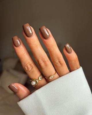 Close-up of a hand with brown nail polish wearing gold rings on a blurred background