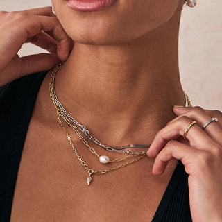 Close-up of a person wearing multiple necklaces with hand adjusting one of them.