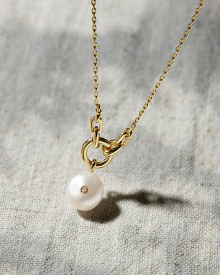 Gold necklace with a pearl pendant on a textured gray background