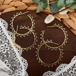Gold hoop earrings on a wooden surface with lace and leaves