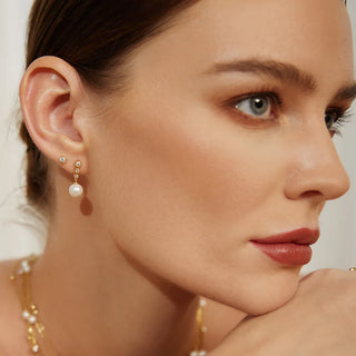 Close-up of a woman wearing pearl earrings and necklace against a neutral background
