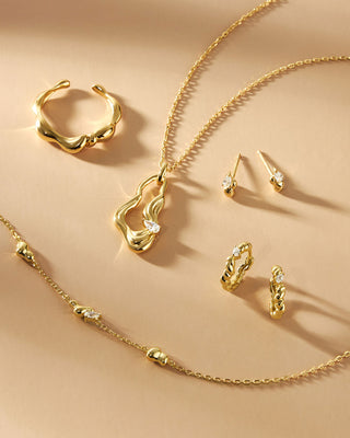 Gold jewellery set including necklace, earrings, and rings on a beige background