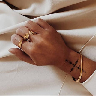 Hand wearing gold rings and a bracelet on a beige fabric background