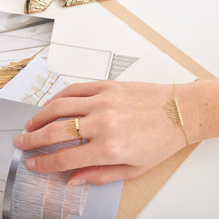 Hand wearing a gold ring and bracelet on a light background