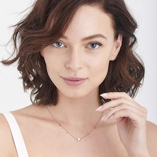 Woman wearing a delicate rose gold necklace against a plain background