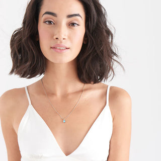 Woman wearing a necklace with a white top on a plain background