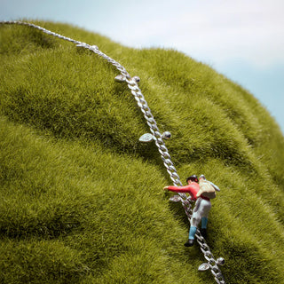 Two small figurines climbing a silver chain on a grassy hill