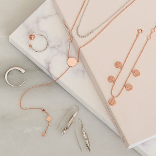 Jewelry set including necklaces and earrings on a marble surface with a beige box.