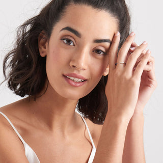 Woman with a neutral expression, wearing a white top, on a plain background