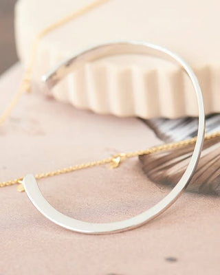Silver bangle and gold necklace on a soft fabric background