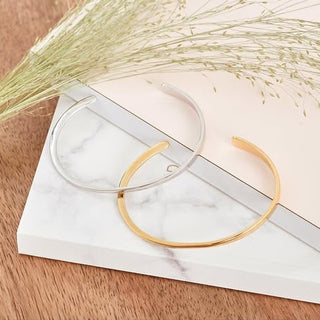 Gold and silver bangles on a marble surface with dried grasses.