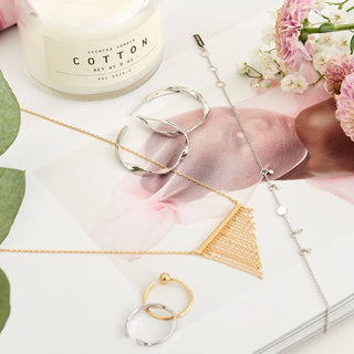 Jewelry set with necklaces and a candle on a decorative surface with flowers.