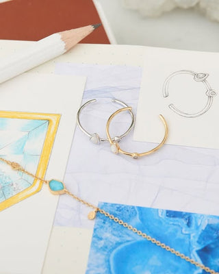Jewelry including hoop earrings and a necklace on a textured surface with a pencil.