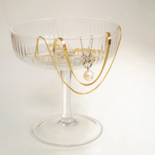 Clear glass dish with gold rim holding a necklace on a light background