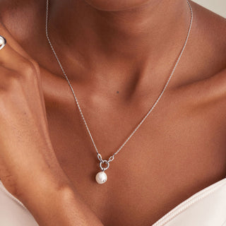 Silver necklace with a pearl pendant on a person wearing a white top.