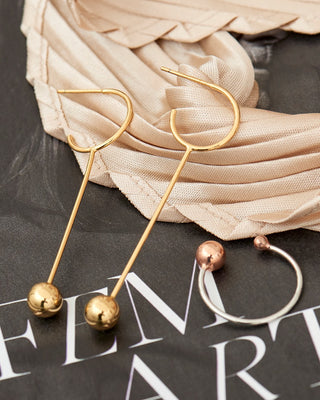 Gold and silver earrings on a textured surface with text in the background
