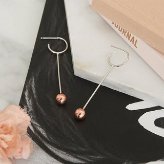 Pair of earrings with rose gold and silver finishes on a black surface.