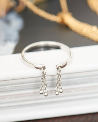 Silver ring with dangling beads on a white surface