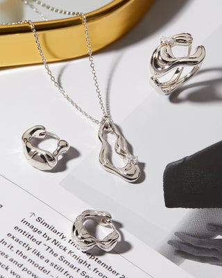 Silver jewelry set including necklace, ring, and earrings on a white surface with a gold mirror in the background.