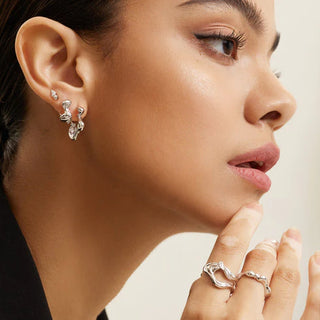 Close-up of a woman wearing silver earrings and rings on a neutral background