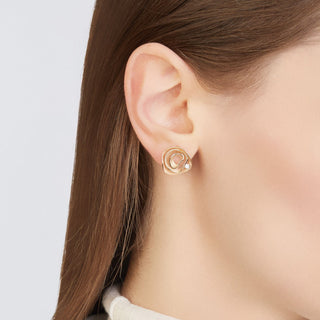 Close-up of a person wearing gold earrings with a plain background