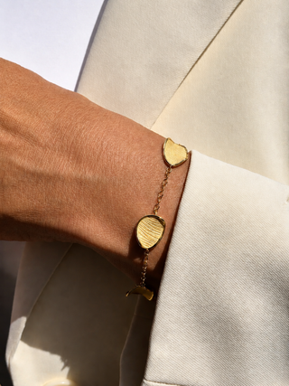 Gold bracelet with heart-shaped charms on a wrist against a neutral background