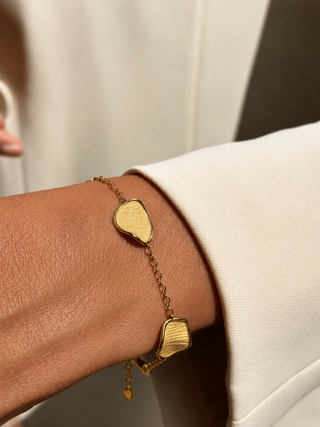 Gold bracelet with organic-shaped textured charms on a wrist against a neutral background