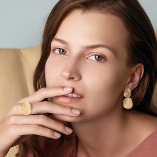 Woman wearing gold earrings and ring with a neutral background