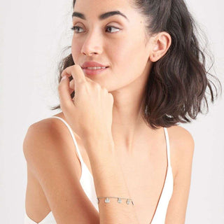 Woman wearing a white tank top with visible jewelry on a plain background