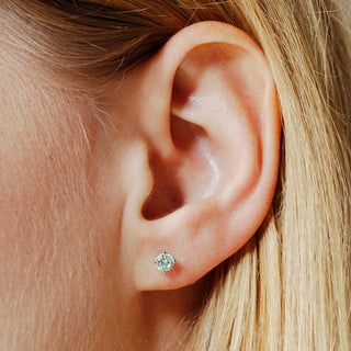 Close-up of an ear wearing a diamond stud earring with blonde hair.