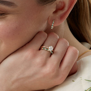 Close-up of a woman's ear wearing a diamond earring and ring, with a blurred background.