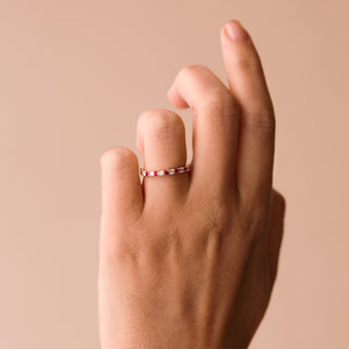 Hand wearing a gold ruby eternity ring on a beige background