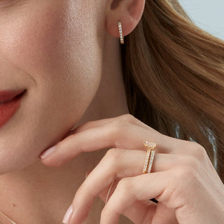 Close-up of a woman wearing gold hoop earrings and rings on a neutral background