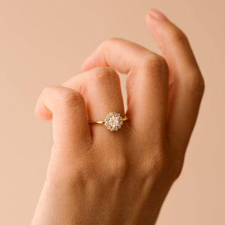 Gold ring with a diamond cluster on a hand against a beige background