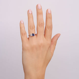 Hand wearing a ring with a blue gemstone on a light gray background