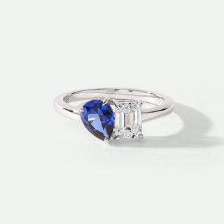 Ring with blue heart-shaped gemstone and clear rectangular gemstone on a white background