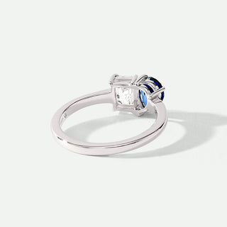 Silver ring with a diamond and blue gemstone on a white background