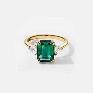 Gold ring with a green gemstone and diamonds on a white background