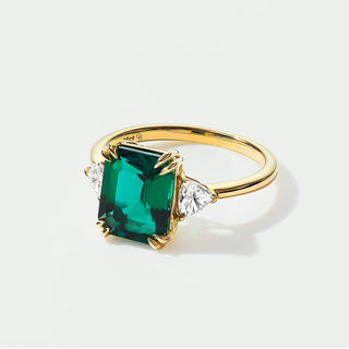 Gold ring with a green gemstone and diamonds on a white background