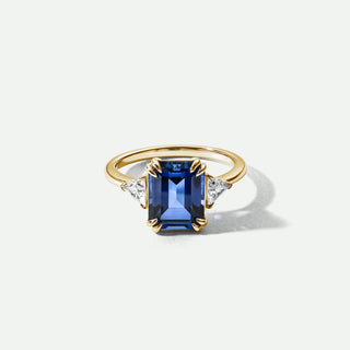 Gold ring with a blue gemstone and diamond accents on a white background